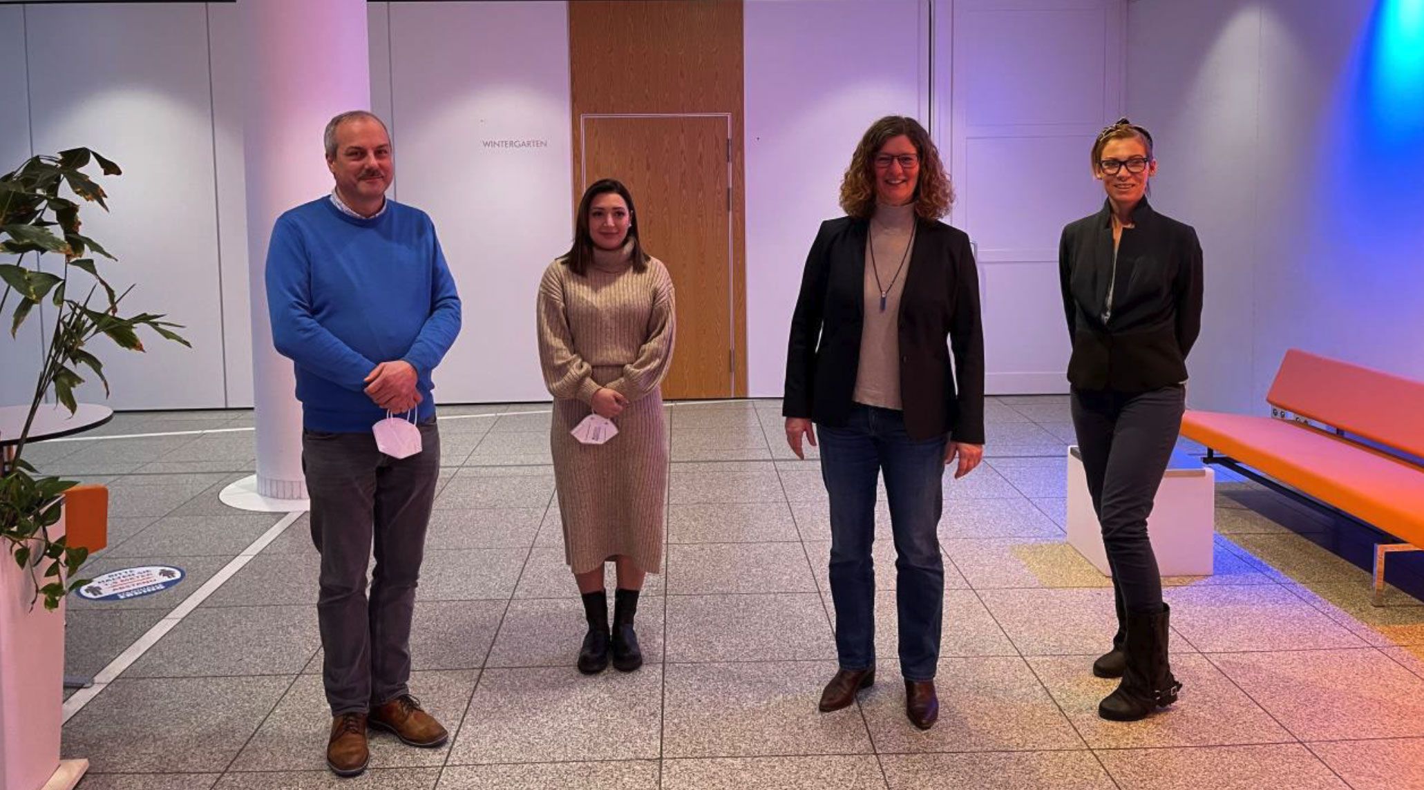 Vier Personen stehen in einem Büro, beleuchtet von blauen und orangefarbenen Lichtern.